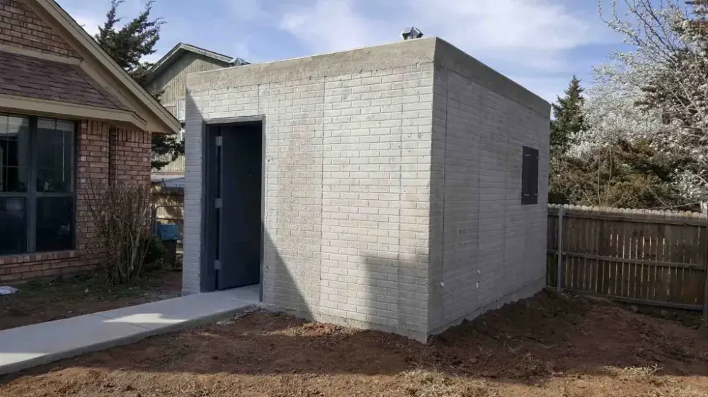 Above-ground brick-textured poured-concrete safe room beside a home